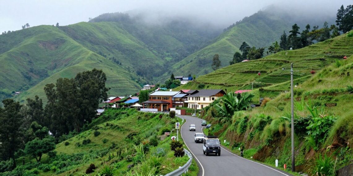 Winding mountain road through a lush green hillside village with colorful houses and misty, forested mountains in the background
